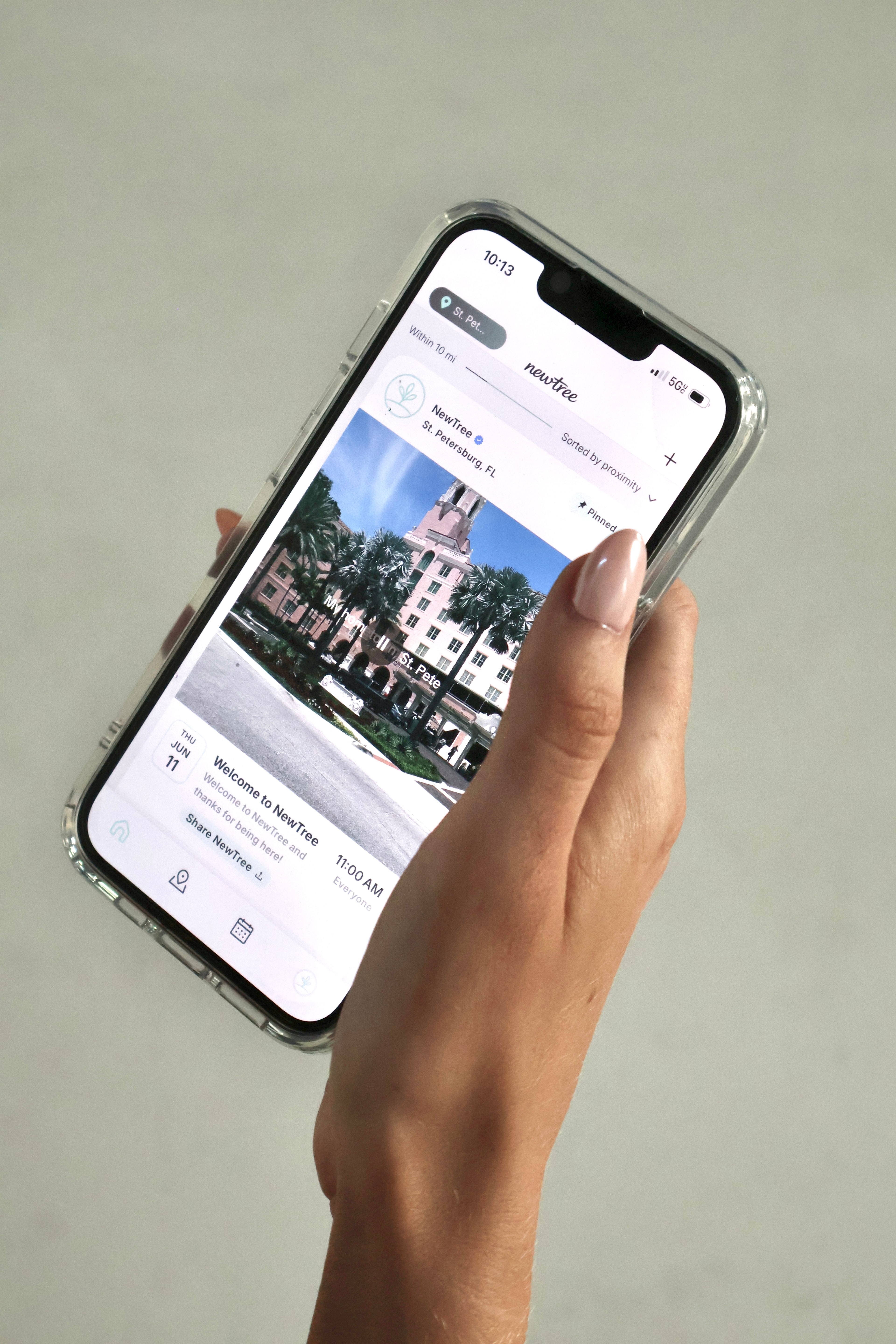 A hand holding a phone showing the NewTree event feed for St. Petersburg, FL